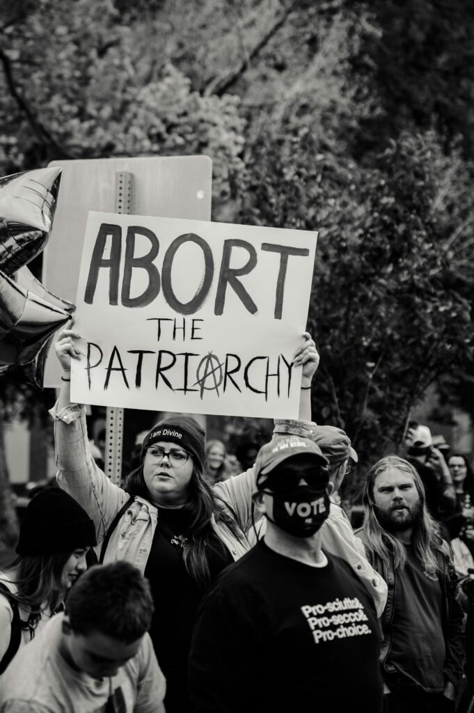 Grayscale Photo of Millennial Woman Holding an Abort the Patriarchy Sign